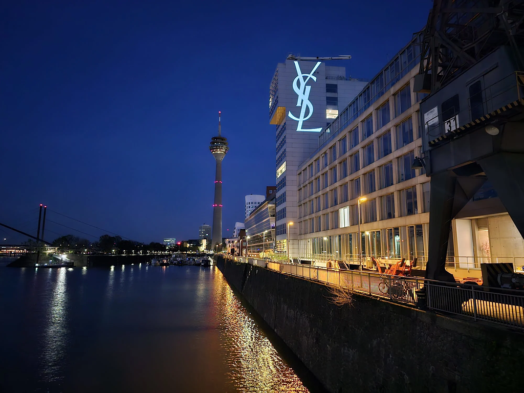 YSL LOVESHINE campaign logo projected onto a building overlooking the Rhine River in Düsseldorf at night